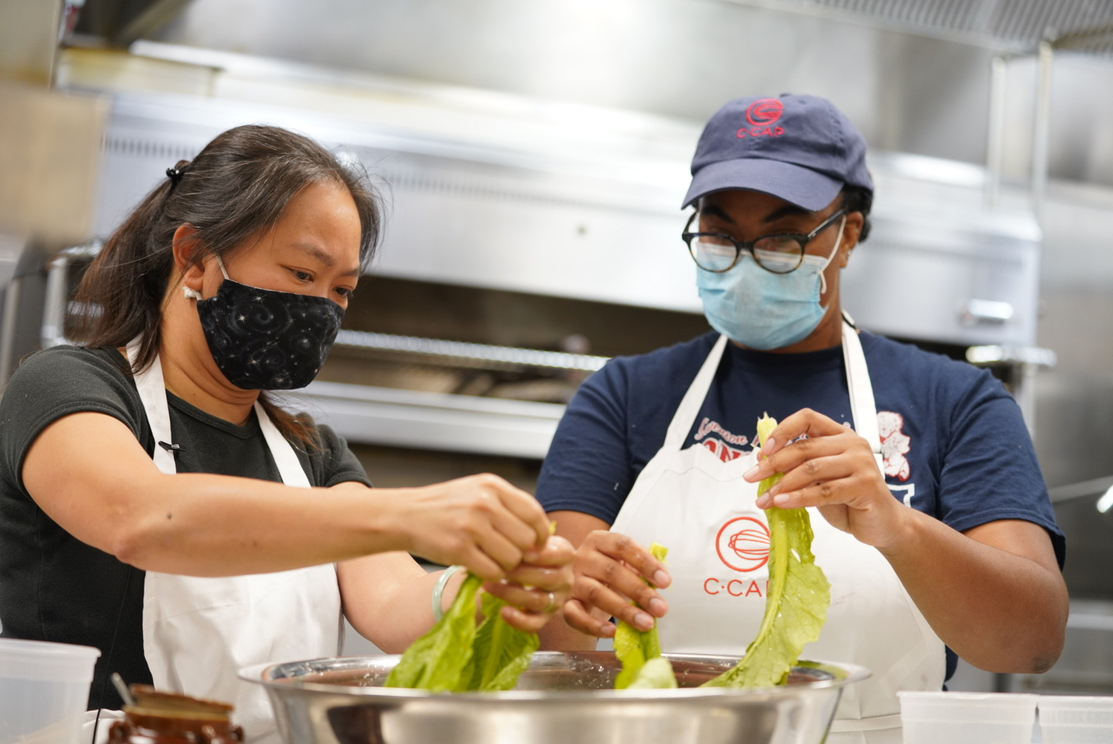 Two people with masks cleaning a bowl of vegetables